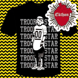 May include: Black t-shirt with a white and gray graphic of a Star Wars Stormtrooper wearing a jersey with the number 00. The text "TROOP STAR" is repeated multiple times on the shirt.