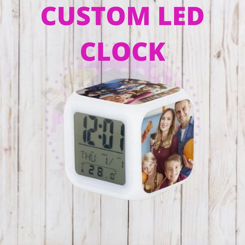 Pode incluir: Rel&oacute;gio LED branco em forma de cubo com um visor digital que mostra a hora 12:01, o dia THU e a data 28. O rel&oacute;gio tem uma foto de uma fam&iacute;lia na frente.