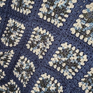 May include: A blue crocheted blanket with a repeating pattern of white, blue, and black squares.