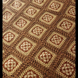 May include: A crocheted throw blanket with a brown and cream color pattern. The blanket is made of squares with a floral design in the center.