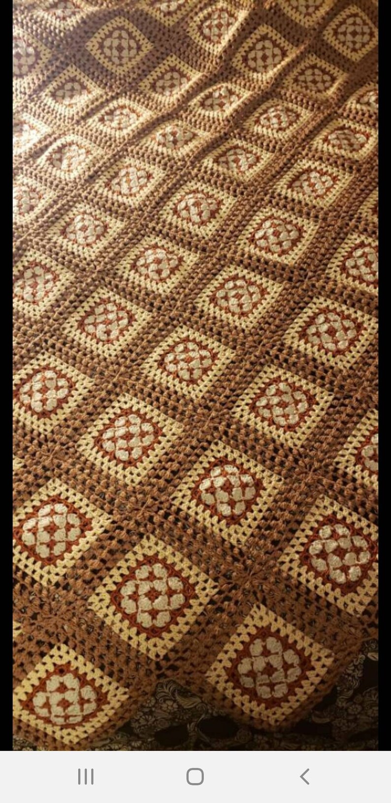 May include: A crocheted throw blanket with a brown and cream color pattern. The blanket is made of squares with a floral design in the center.