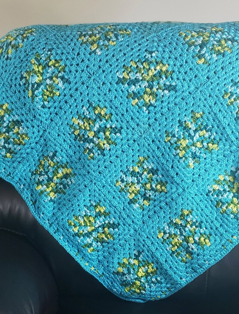 May include: A crocheted blanket with a diamond pattern in shades of turquoise, green, and white.