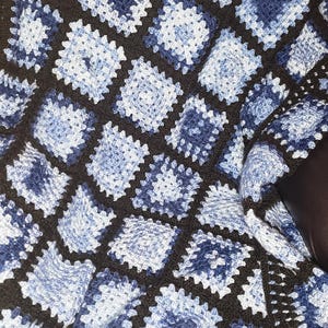May include: A crocheted blanket with a black and blue pattern. The blanket is made of squares with a granny stitch design.