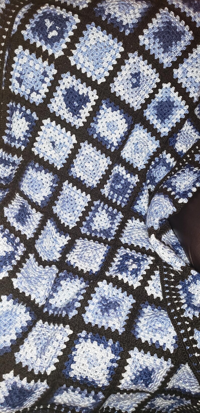 May include: A crocheted blanket with a black and blue pattern. The blanket is made of squares with a granny stitch design.