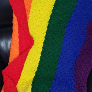 May include: A crocheted rainbow blanket with a textured pattern. The blanket is folded and draped over a black chair.