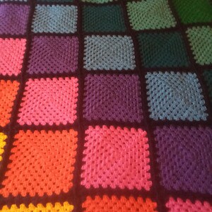 May include: A colorful crochet blanket with squares in various shades of green, blue, purple, pink, red, orange, and yellow. The squares are outlined in black.