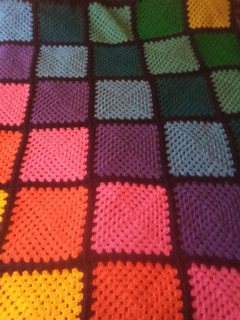 May include: A colorful crochet blanket with squares in various shades of green, blue, purple, pink, red, orange, and yellow. The squares are outlined in black.