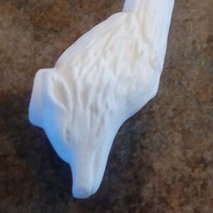 May include: A white, carved sculpture of a wolf's head and neck. The sculpture has a detailed, textured surface and is set against a brown background. The wolf's head is in profile, with its snout and ear clearly defined.