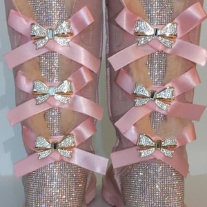 May include: Pink suede boots with a sparkly finish and multiple pink satin bows with rhinestone accents.