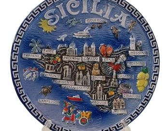 May include: A blue decorative plate featuring a map of Sicily with city names and landmarks. The plate has a white Greek key border and the word "SICILIA" at the top. Includes images of boats, landmarks, and local produce.