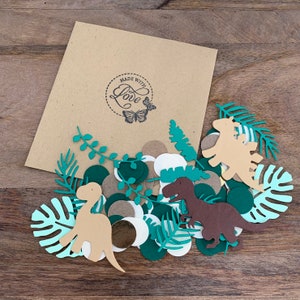Op de afbeelding: Een bruine papieren envelop met een "Made with Love" stempel en een vlinderontwerp. De envelop bevat groene, bruine en witte confetti met dinosaurussen en bladeren.