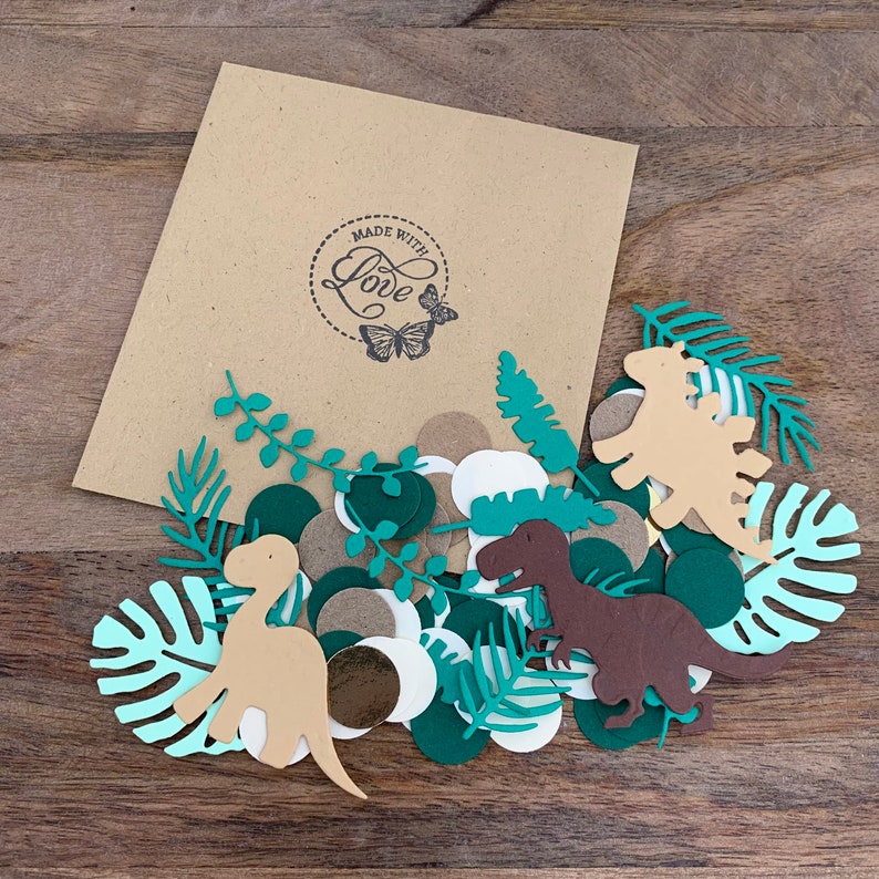 Op de afbeelding: Een bruine papieren envelop met een "Made with Love" stempel en een vlinderontwerp. De envelop bevat groene, bruine en witte confetti met dinosaurussen en bladeren.
