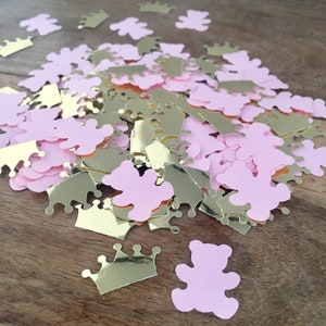 Op de afbeelding: Roze teddybeer- en gouden kroonconfetti verspreid op een houten oppervlak. De gouden confetti heeft een metallic glans, terwijl de teddybeer confetti zachtroze is.