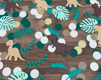 Könnte beinhalten: Eine Sammlung grüner, brauner und goldener Konfetti mit Dinosaurier- und tropischen Blattformen. Das Konfetti ist perfekt für eine Dinosaurier-Party.