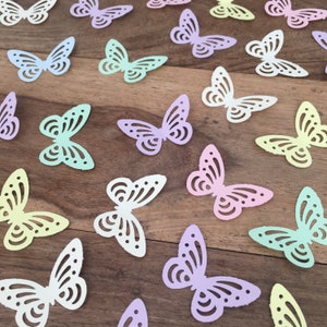 Op de afbeelding: Assortiment van pastelkleurige papieren vlinders met ingewikkelde uitgesneden ontwerpen. De vlinders zijn verspreid over een houten oppervlak.