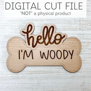 May include: A wooden dog bone shaped sign with the text "hello I'M WOODY" engraved on it. The sign is a digital cut file, not a physical product.