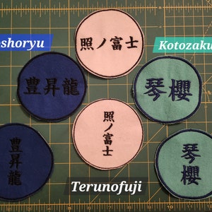 May include: Six round embroidered patches with Japanese text. The patches are blue, green, and pink. The text on the patches reads "Hoshoryu", "照ノ富士", "Kotozakura", "豊昇龍", "琴櫻", and "Terunofuji".