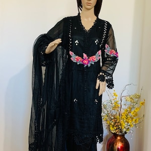 May include: A black sheer dress with floral embroidery and lace detailing. The dress has a long sleeve and a flowing silhouette. The dress is paired with a matching black sheer dupatta.