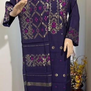 May include: A dark purple long-sleeved tunic featuring gold and magenta geometric patterns, paired with a matching shawl and solid magenta trousers. The tunic has a scoop neckline and gold metallic detailing along the hem and sleeves.