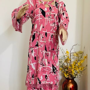 May include: A pink and black patterned two-piece outfit with long sleeves and a geometric design. The top has a cut-out detail at the neckline. The pants have a wide leg.