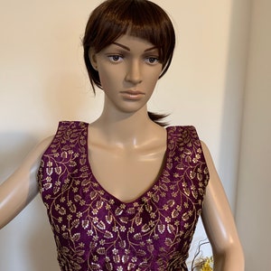 Puede incluir: Una blusa morada sin mangas con bordados dorados con un patrón floral.