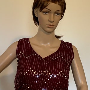 Puede incluir: Una blusa sin mangas de color burdeos con escote en V y lentejuelas plateadas.