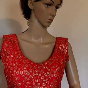 May include: A red sleeveless blouse with a V-neckline and gold floral embroidery. The embroidery features sequins and beads.
