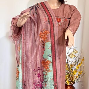 Op de afbeelding: Een roze en groene jurk met bloemenprint en een bijpassende dupatta. De jurk heeft een ronde hals en korte mouwen. De dupatta heeft een bloemenrand en een roze en groene bloemenprint.
