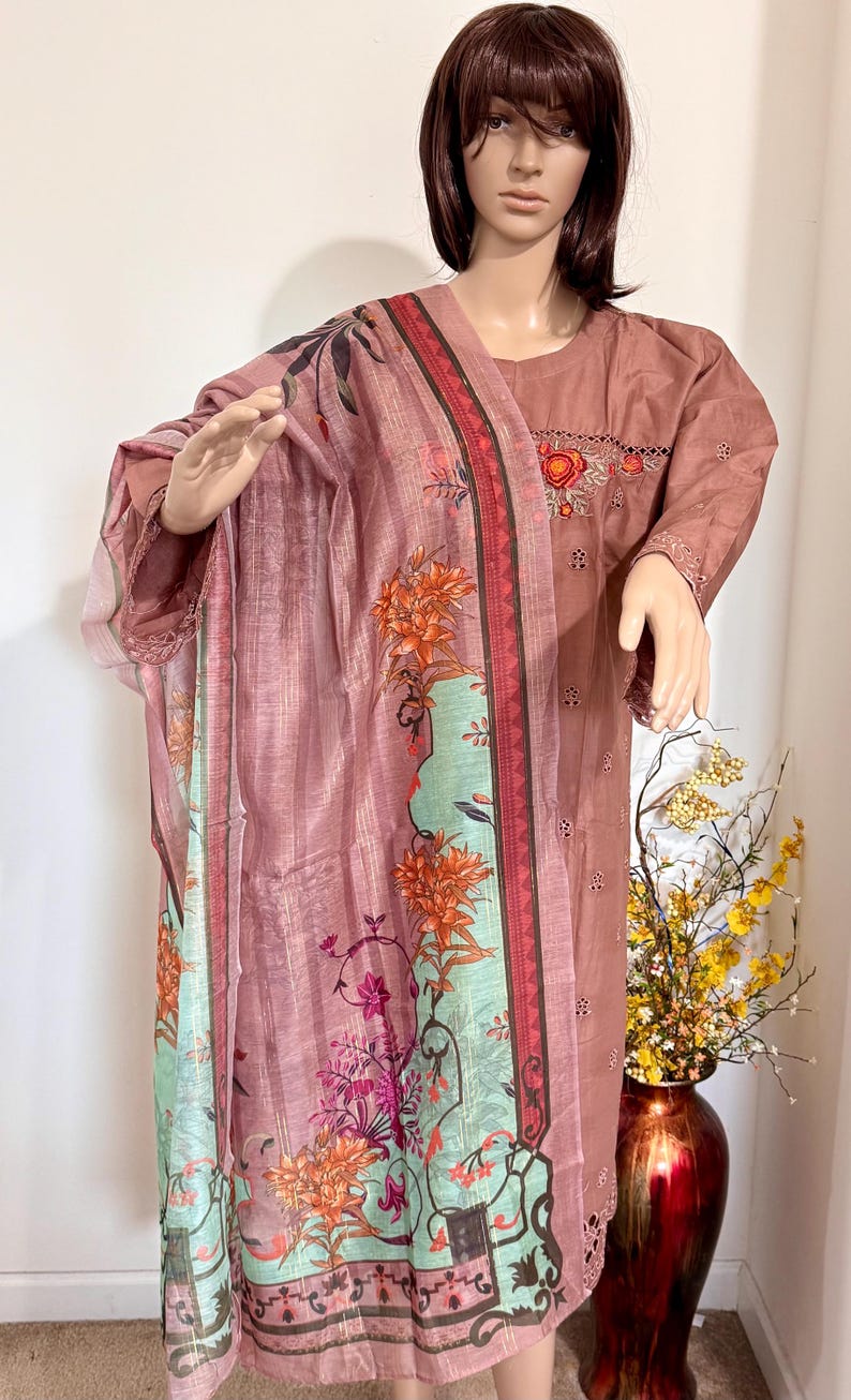 Op de afbeelding: Een roze en groene jurk met bloemenprint en een bijpassende dupatta. De jurk heeft een ronde hals en korte mouwen. De dupatta heeft een bloemenrand en een roze en groene bloemenprint.