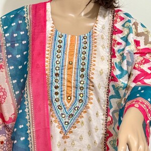 May include: A white cotton tunic with a colorful embroidered neckline and a pink dupatta. The embroidery features a geometric pattern with gold, blue, and orange accents.