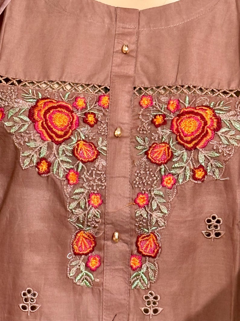 Op de afbeelding: Een bruin katoenen top met een bloemenborduursel. De borduursels bevatten roze, oranje en rode bloemen met groene bladeren. De top heeft een knoopsluiting.