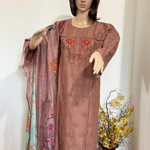 Op de afbeelding: Een bruine geborduurde jurk met een dupatta met bloemenprint. De jurk heeft een ronde halslijn en lange mouwen. De dupatta is lichtroze en groen met bloemenontwerpen.
