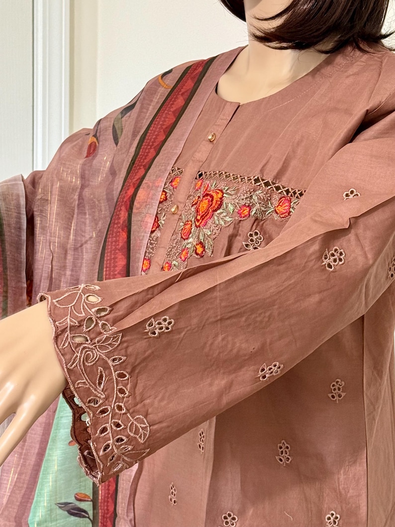 Op de afbeelding: Een stoffig roze geborduurd top met een bloemenontwerp. De top heeft een ronde halslijn en lange mouwen met kantdetails. De top is gemaakt van een zachte, lichtgewicht stof.