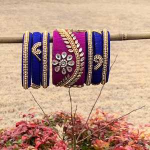 Puede incluir: Un conjunto de pulseras coloridas con diseños intrincados. Las pulseras están hechas de hilo de seda y decoradas con adornos dorados y plateados. Las pulseras están dispuestas en una pila, con la pulsera morada en la parte superior y las pulseras azules debajo.