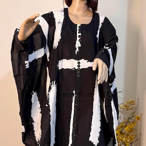 May include: Black and white abstract print tunic dress with a button-up front. The dress has a loose, flowing silhouette and a slightly asymmetrical hemline.
