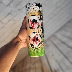 May include: A stainless steel tumbler with a green, yellow, and black design featuring soccer balls and the names "Ava" and "Isla".