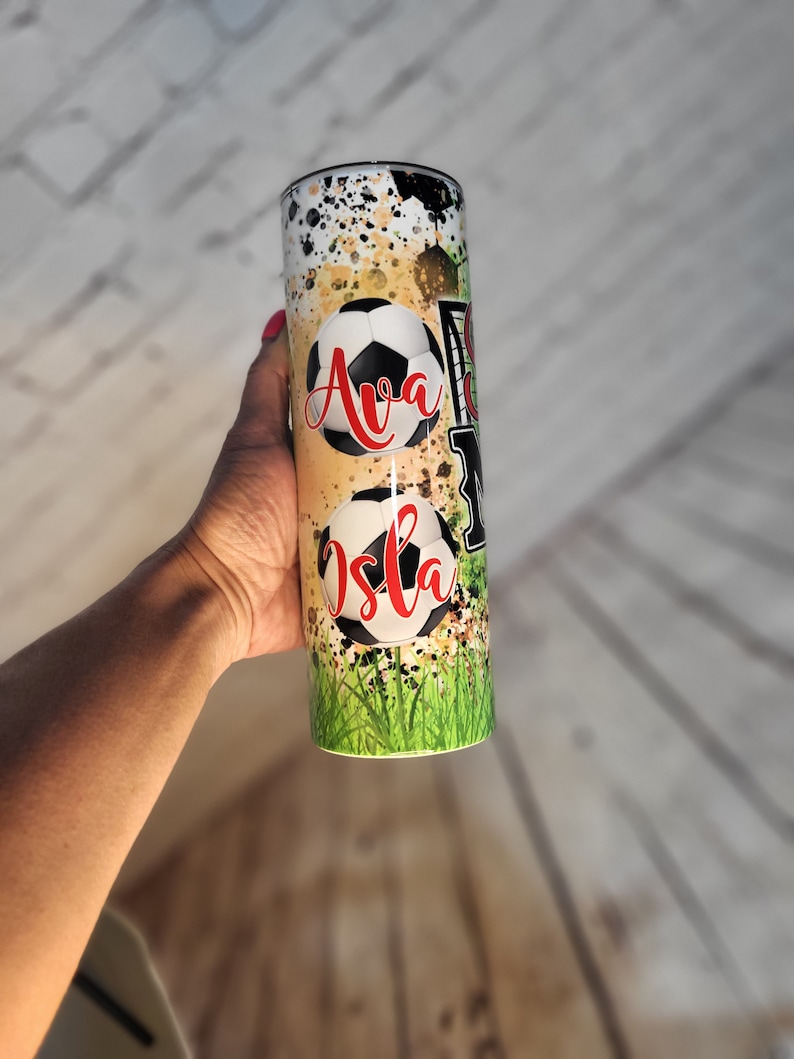 May include: A stainless steel tumbler with a green, yellow, and black design featuring soccer balls and the names "Ava" and "Isla".
