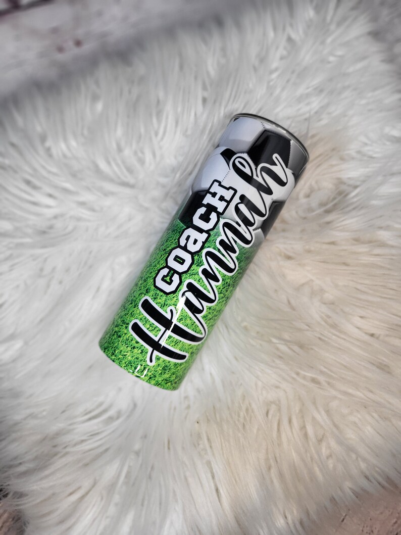 K&ouml;nnte beinhalten: Ein gr&uuml;ner und schwarzer Edelstahlbecher mit einem Fu&szlig;balldesign und dem Text "All Coach Mom".