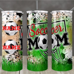 May include: A green, white, and black tumbler with a soccer ball and the words "Soccer Mom" on it. The tumbler has a splatter paint design and a green grass background.