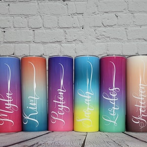 Puede incluir: Diez vasos de acero inoxidable personalizados con un diseño degradado de arcoíris. Cada vaso presenta un nombre diferente en letras blancas: Alisha, Millie, Myla, Krin, Keyton, Sarah, Less, Gretchen, Mary y Gail.