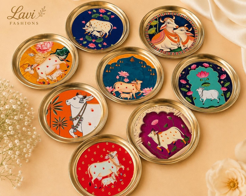 May include: A collection of eight circular brass-rimmed coasters featuring colorful illustrations of cows and calves amidst lotus flowers. Each coaster displays distinct artistic scenes with vibrant backgrounds in blue, orange, red, and magenta.