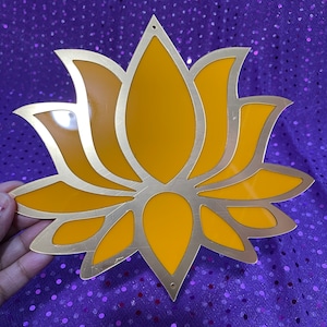 May include: A gold-colored metal lotus flower cutout with a yellow background. The lotus flower is a popular symbol of purity, enlightenment, and rebirth.