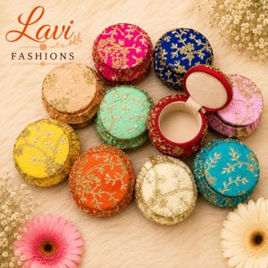 May include: A collection of round, fabric-covered jewelry boxes in various colors including pink, blue, peach, green, yellow, orange, cream, and turquoise, each featuring gold floral embroidery. One red box is open, revealing a beige interior.