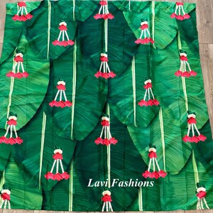 May include: A green fabric backdrop with a repeating pattern of banana leaves and red flower garlands. The fabric has the text "Lavi Fashions" printed in white.