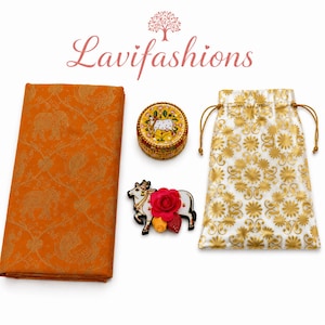 May include: An orange fabric with gold elephant and paisley patterns, a round decorative box, a cow-shaped brooch with a red flower, and a white drawstring bag with gold floral designs. The text "Lavifashions" is at the top.