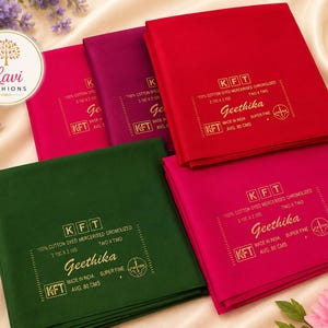 May include: Four folded fabric squares in red, dark green, magenta, and pink. Each piece features gold printed text including KFT, Geethika, 100% cotton dyed mercerised, 2.10m x 2.10m, and made in India. A Lavi Fashions logo is visible in the corner.