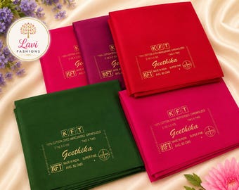 May include: Four folded fabric squares in red, dark green, magenta, and pink. Each piece features gold printed text including KFT, Geethika, 100% cotton dyed mercerised, 2.10m x 2.10m, and made in India. A Lavi Fashions logo is visible in the corner.