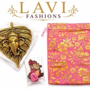 May include: A gold-colored metal leaf-shaped wall hanging with a detailed elephant head design. A small, packaged figurine of an elephant god and a pink floral drawstring bag with gold floral patterns are also present.