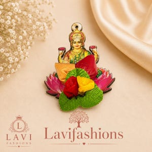 May include: A decorative brooch featuring a central illustration of a deity with gold jewelry and a crown, surrounded by layered fabric petals in red, yellow, and green, set against a pink lotus-shaped base with a small hanging loop at the top.