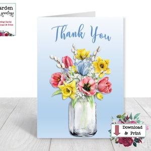 Pode incluir: Um cartão de agradecimento imprimível com uma ilustração em aquarela de um buquê de flores da primavera em um frasco de vidro. As flores são amarelas, rosas e azuis. O cartão tem um fundo azul claro e o texto "Obrigado" em uma fonte cursiva.
